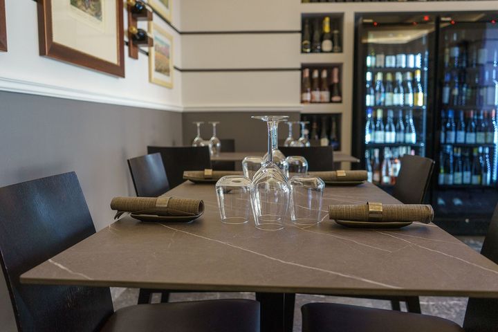 Tavolo da ristorante moderno apparecchiato con bicchieri da vino, posate e un refrigeratore per il vino sullo sfondo.