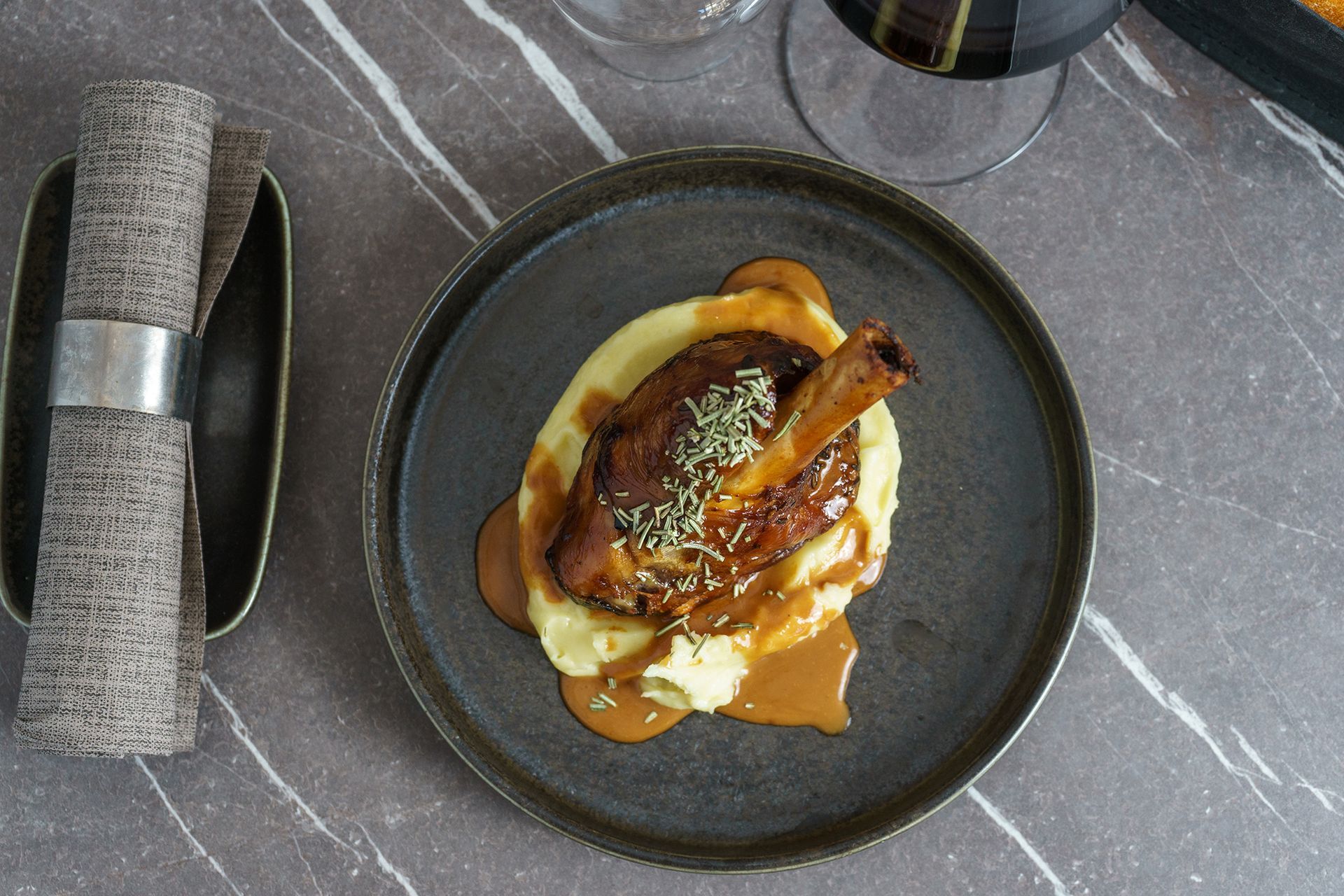 Dessert gourmet servito con salsa al caramello su un piatto scuro, accanto a un tovagliolo arrotolato su un tavolo di marmo.