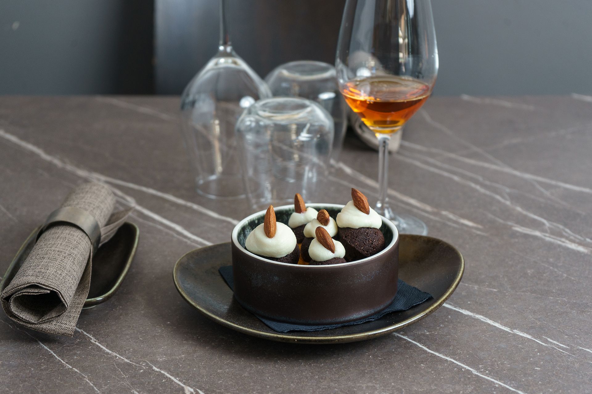Dessert al cioccolato in una ciotola scura con un bicchiere di vino ambrato su un tavolo di marmo.