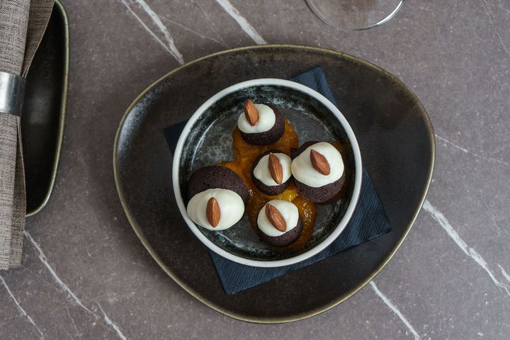Dessert in una ciotola nera guarnito con crema bianca e noci su un piatto scuro.