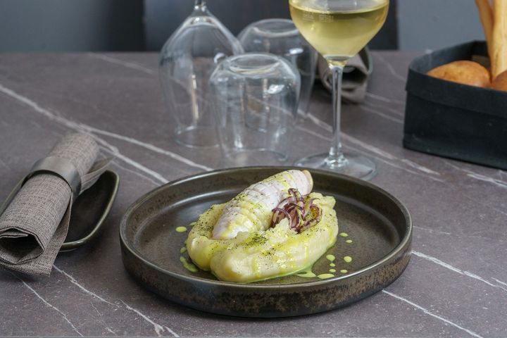Dessert servito su un tavolo scuro con calice da vino, caraffa d'acqua, tovagliolo e cestino del pane nelle vicinanze.