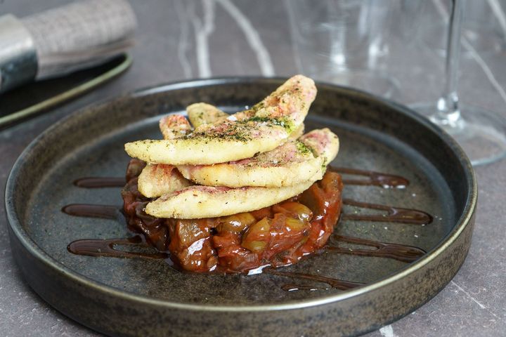 Fette di mela impilate su un dessert sopra una salsa al caramello su un piatto scuro, con una spolverata di zucchero a velo.