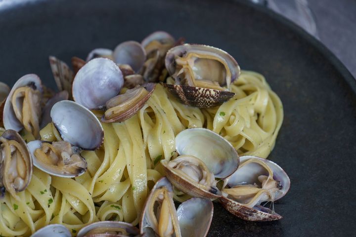 Pasta alle vongole in una ciotola scura, guarnita con erbe aromatiche.