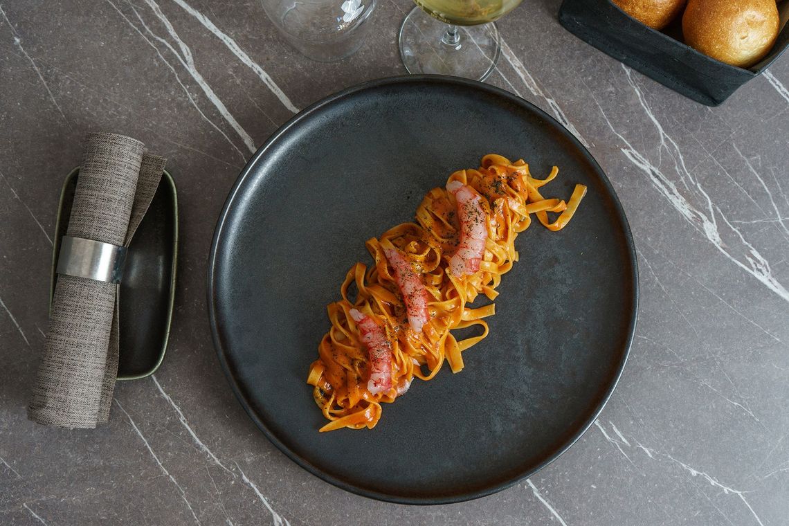 Pasta al sugo di pomodoro servita in un piatto scuro, con tovagliolo piegato e posate su un tavolo di marmo grigio.