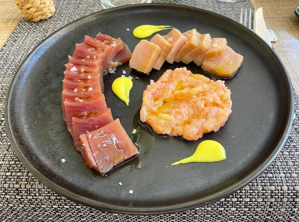 Assortimento di sushi e sashimi su un piatto nero con decorazioni di salsa gialla.