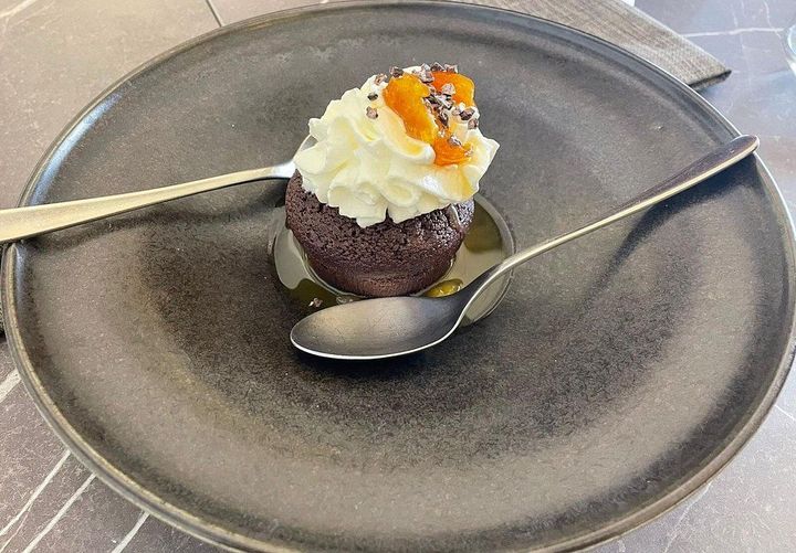 Piccolo dessert al cioccolato con panna montata, servito su un piatto grigio, con due cucchiaini accanto.