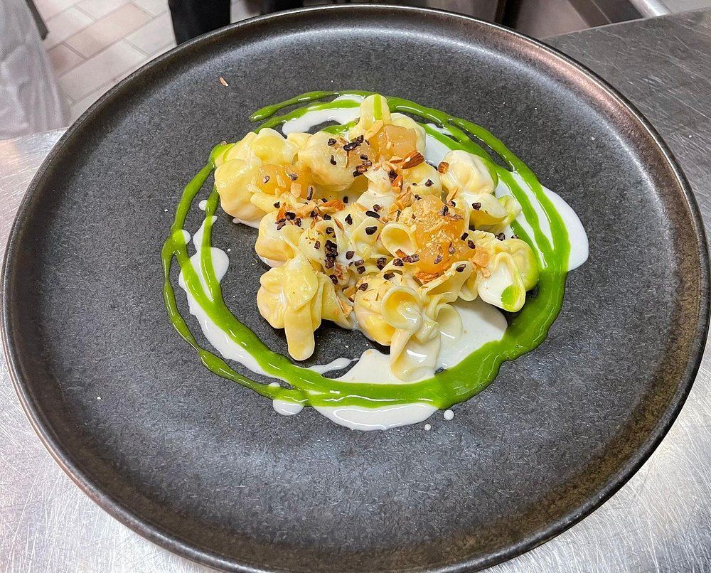 Ciotola nera con pasta cremosa, vortice di salsa verde e guarnizione di sesamo nero su un tavolo