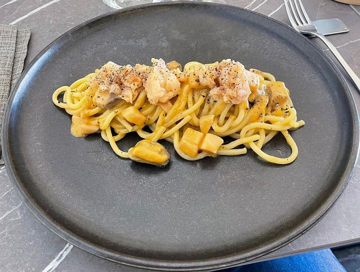 Pasta al salmone su un piatto scuro, guarnita con formaggio grattugiato, su un tavolo.