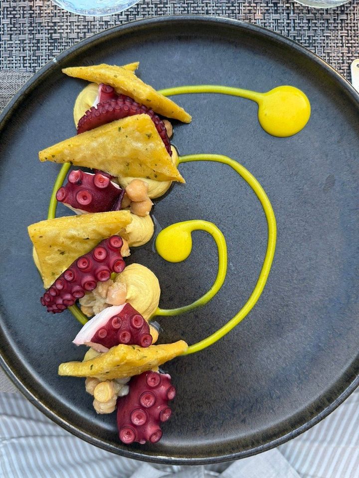 Dessert presentato in modo artistico con salsa gialla, pasta frolla triangolare e frutta rosa su un piatto scuro.