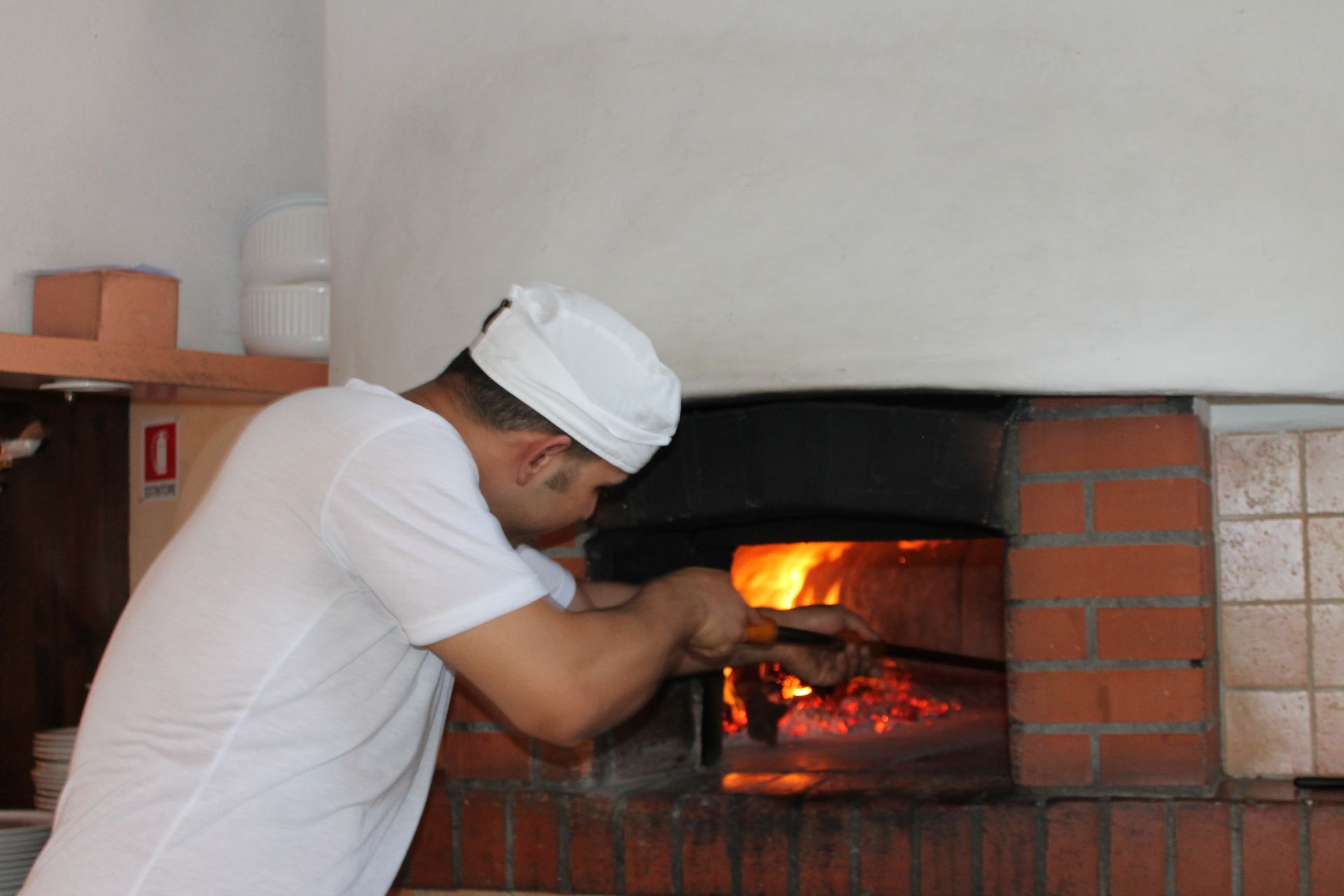 Una persona vestita di bianco si occupa di un forno per pizza con le fiamme accese.
