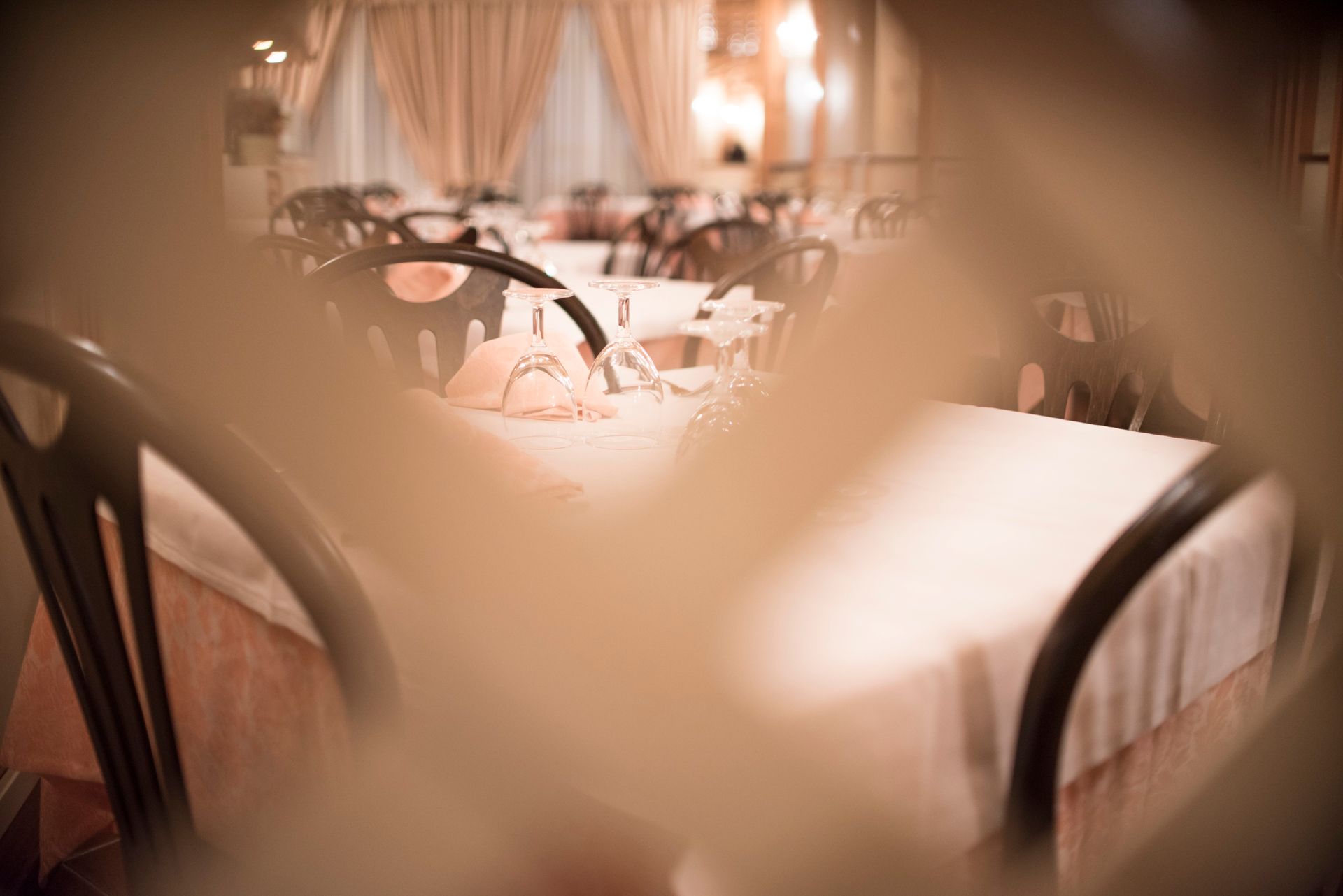 Sala da pranzo del ristorante con tavoli apparecchiati per gli ospiti, vista attraverso un primo piano sfocato.