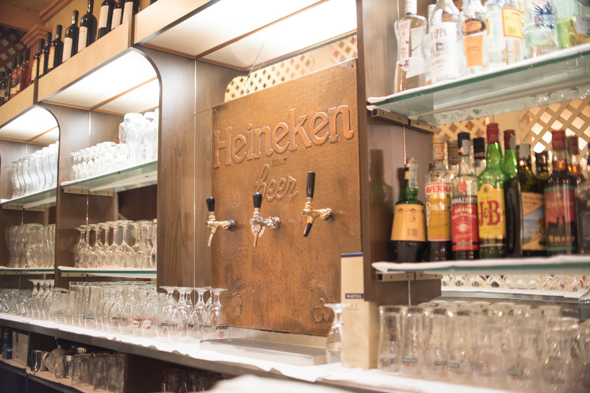 Bar con spine di birra Heineken, bicchieri e bottiglie di liquore sugli scaffali.