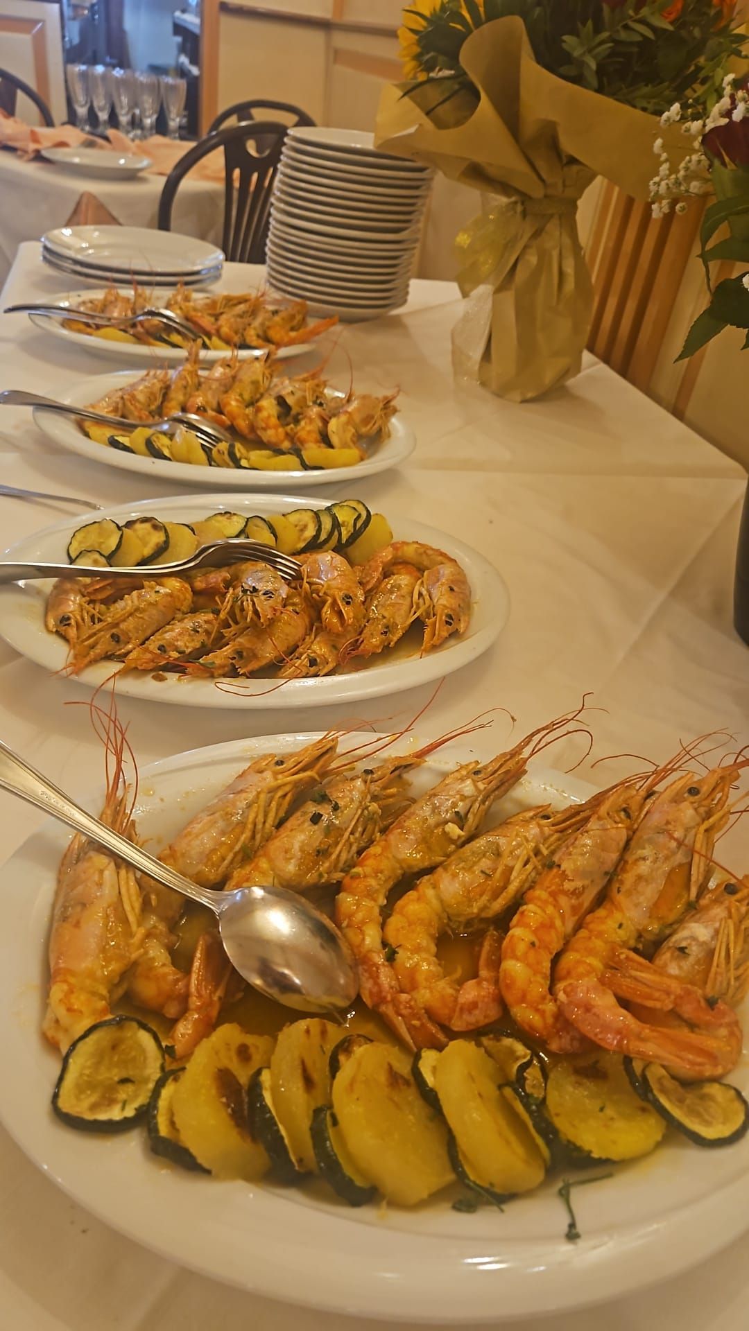 Piatti di gamberi cotti e zucchine grigliate su un tavolo bianco.