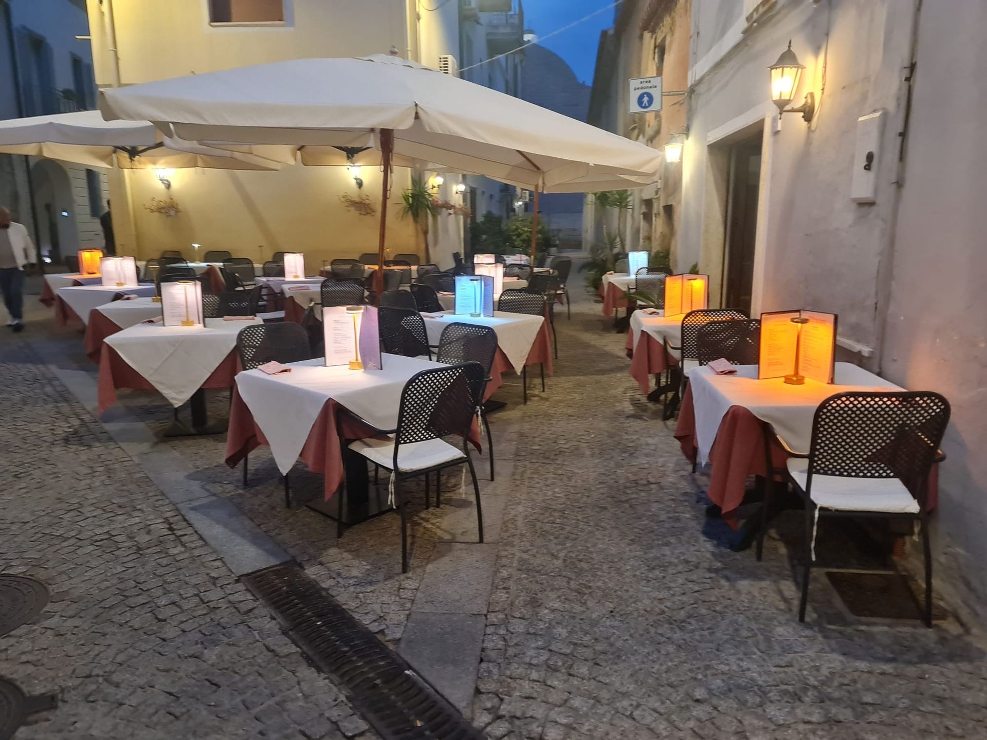 Ristorante all'aperto con ombrelloni bianchi, tavoli e sedie. Diverse persone sono sedute.