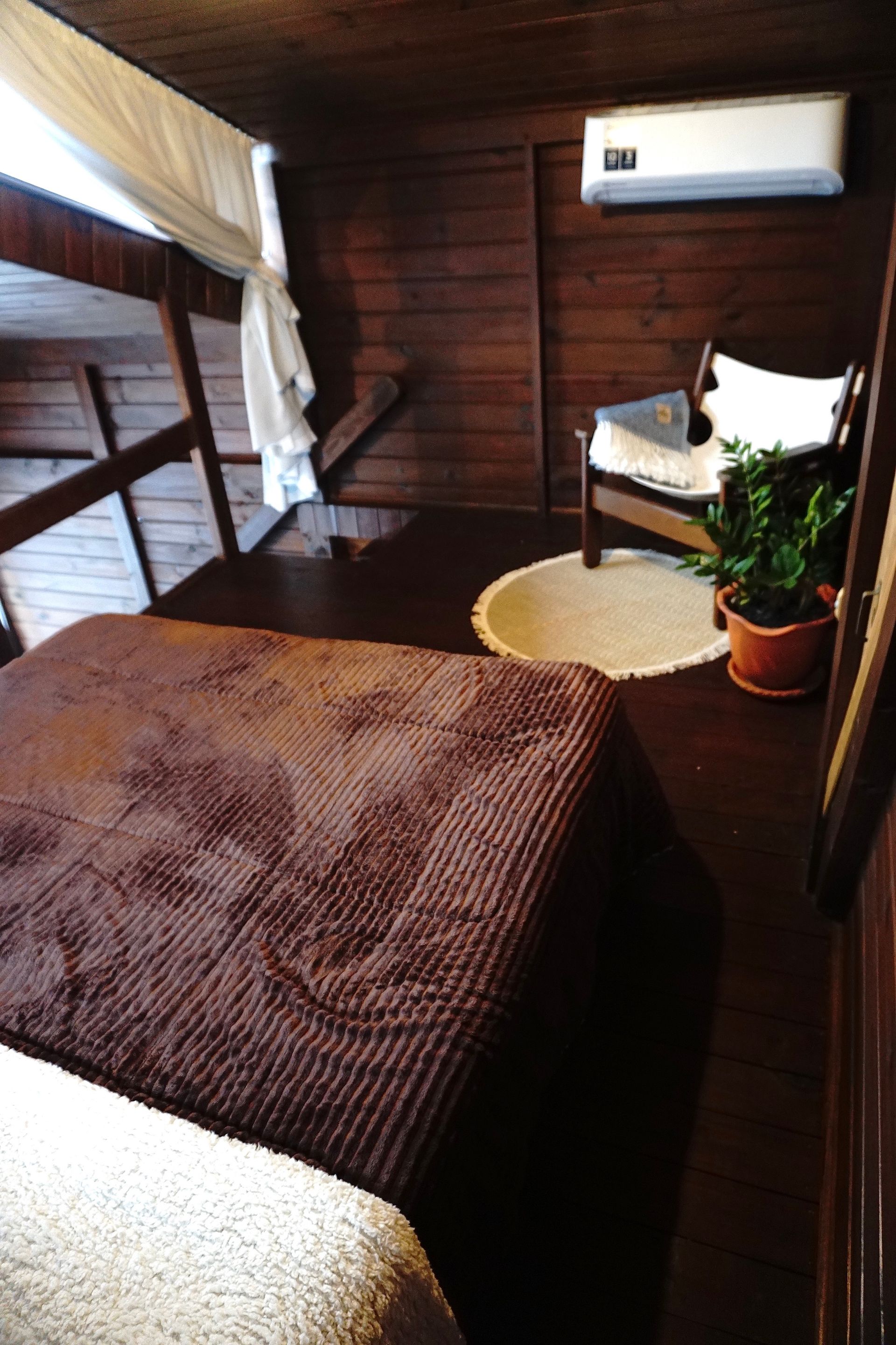 Interior rústico de loft em madeira com uma pequena mesa, cadeiras e grandes janelas com vista para a vegetação.