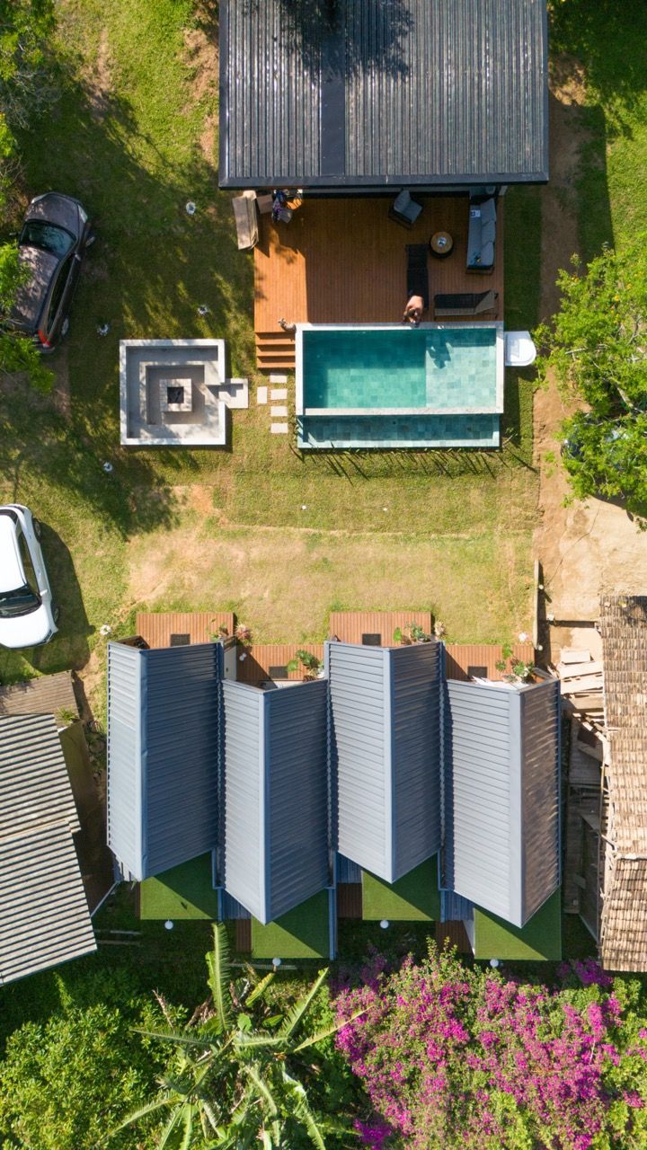 Vista aérea de um quintal com piscina, pátio e várias construções cobertas, cercado por vegetação.