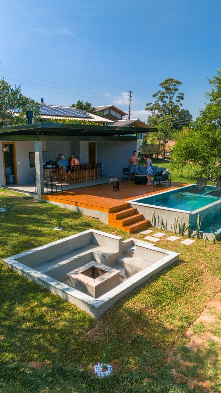 Quintal com piscina pequena, área de estar externa e um deck elevado ao lado de um gramado.