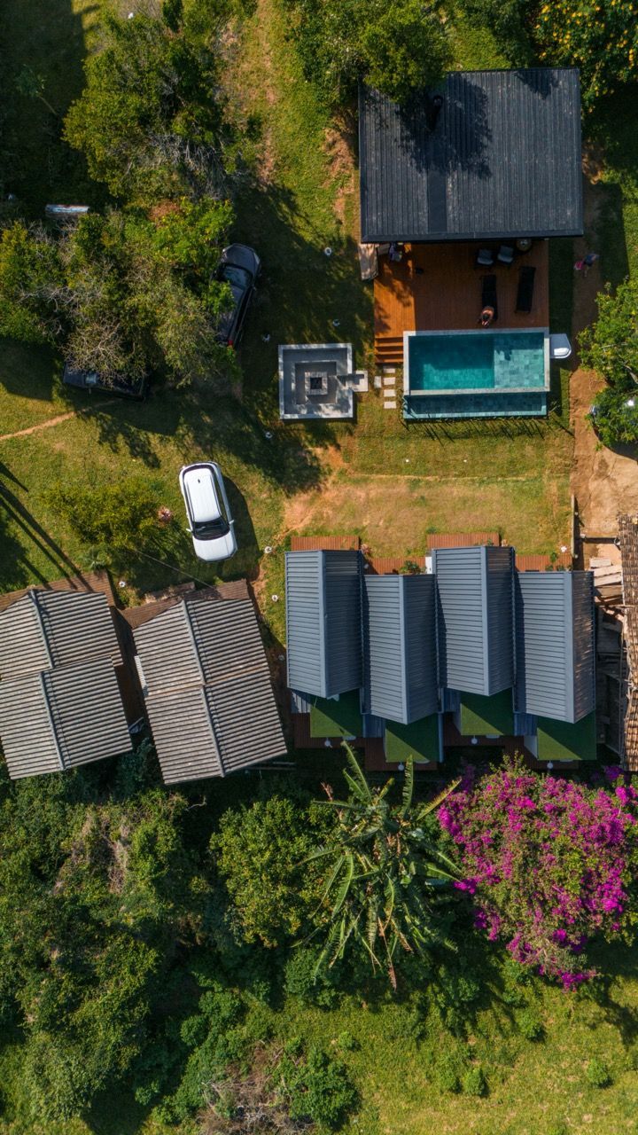 Vista aérea de uma casa com piscina turquesa, carro branco e vegetação tropical densa.