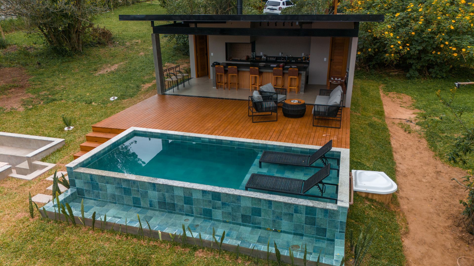 Terraço externo com uma pequena piscina revestida de azulejos, espreguiçadeiras e uma área de estar coberta com vista para a vegetação.