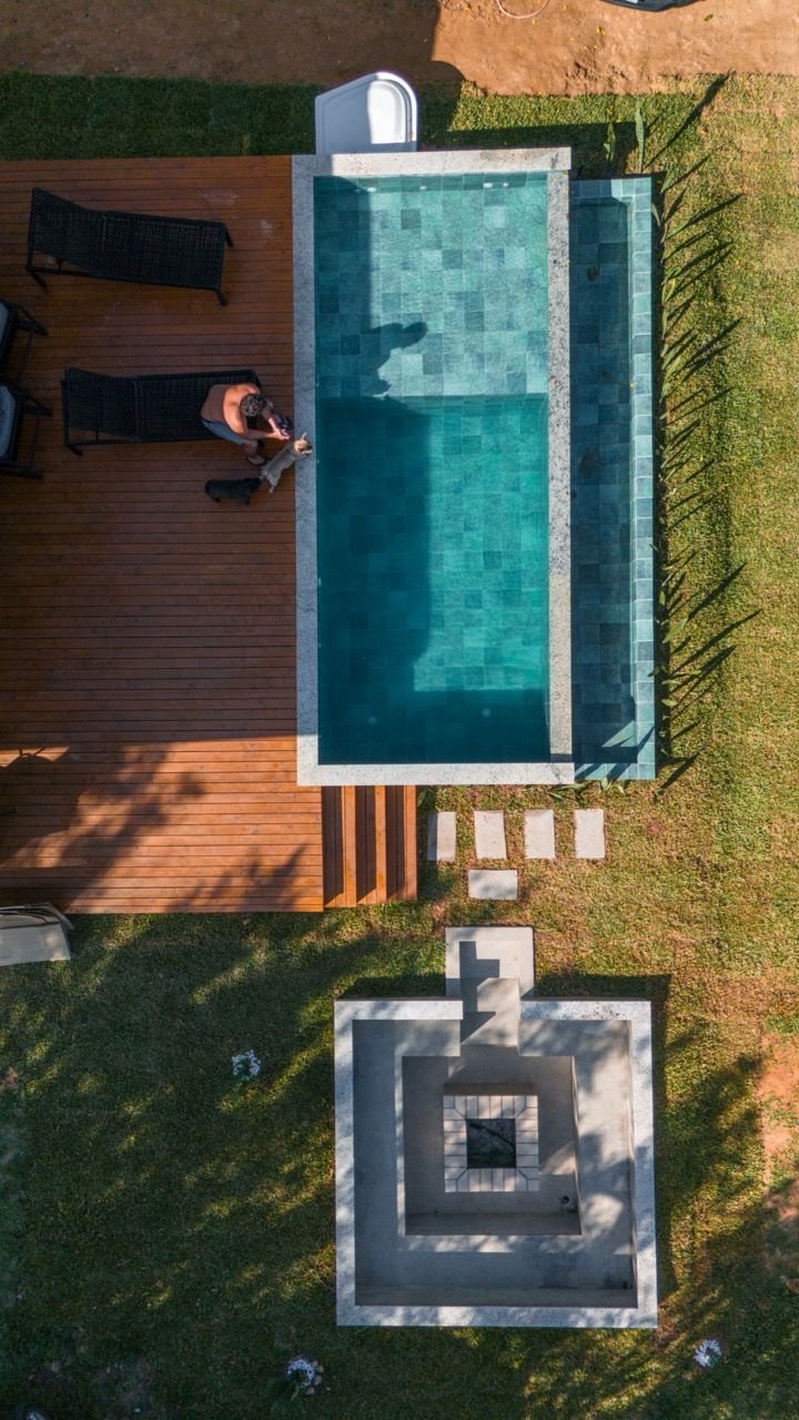 Vista aérea de uma piscina no quintal com deck de madeira, uma pessoa relaxando nas proximidades e uma fogueira abaixo.