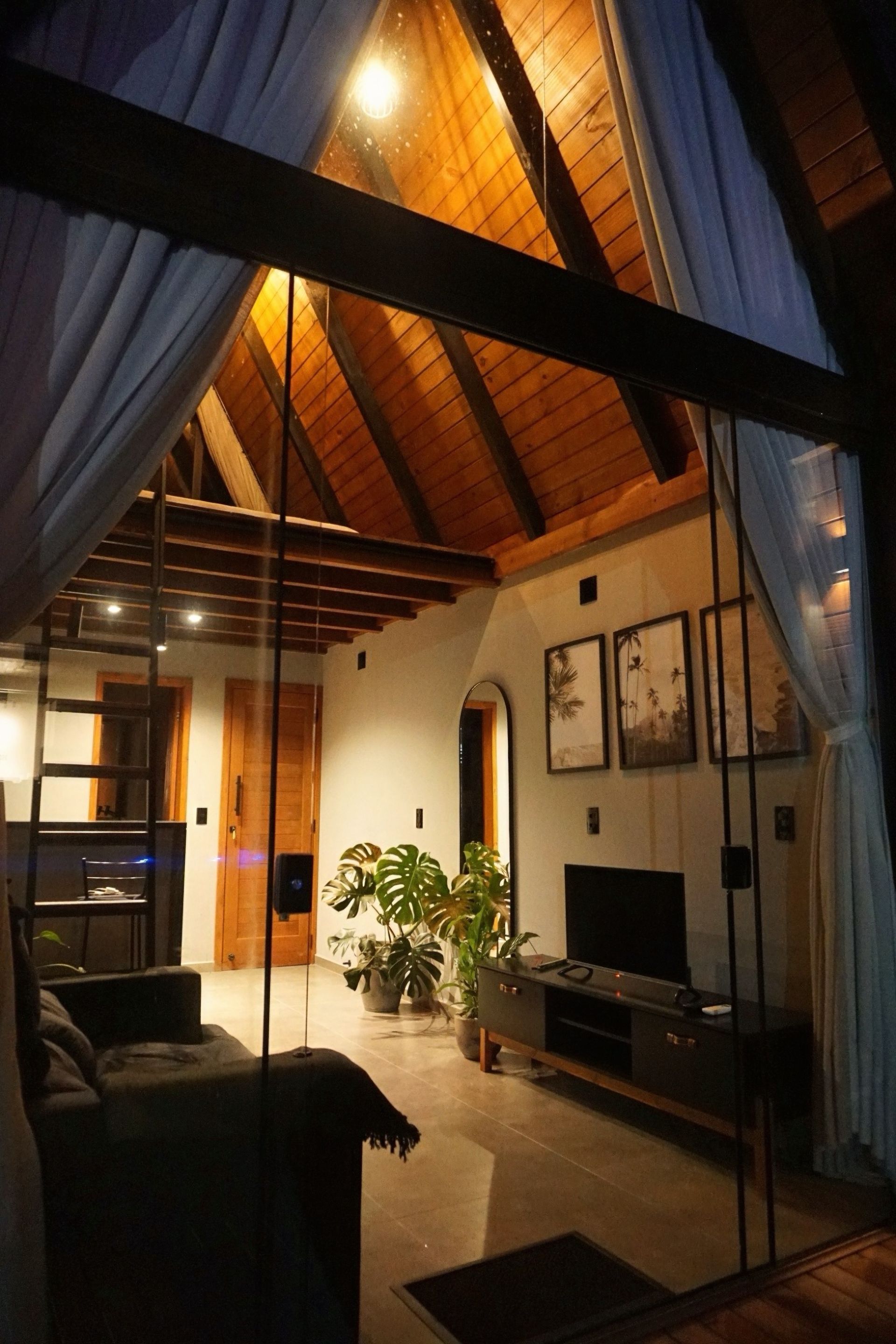 Sala de estar aconchegante em estilo loft, com teto alto de madeira, cortinas azuis, paredes brancas e iluminação quente de abajures.