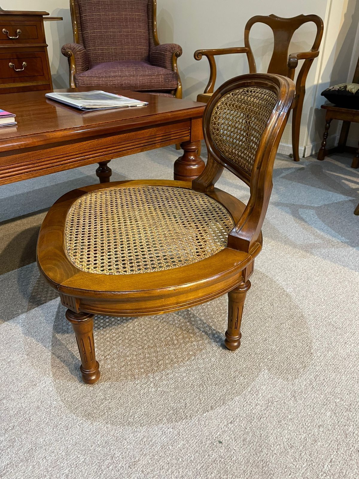 Una silla de madera con asiento de mimbre está sentada en una sala de estar junto a una mesa de café.