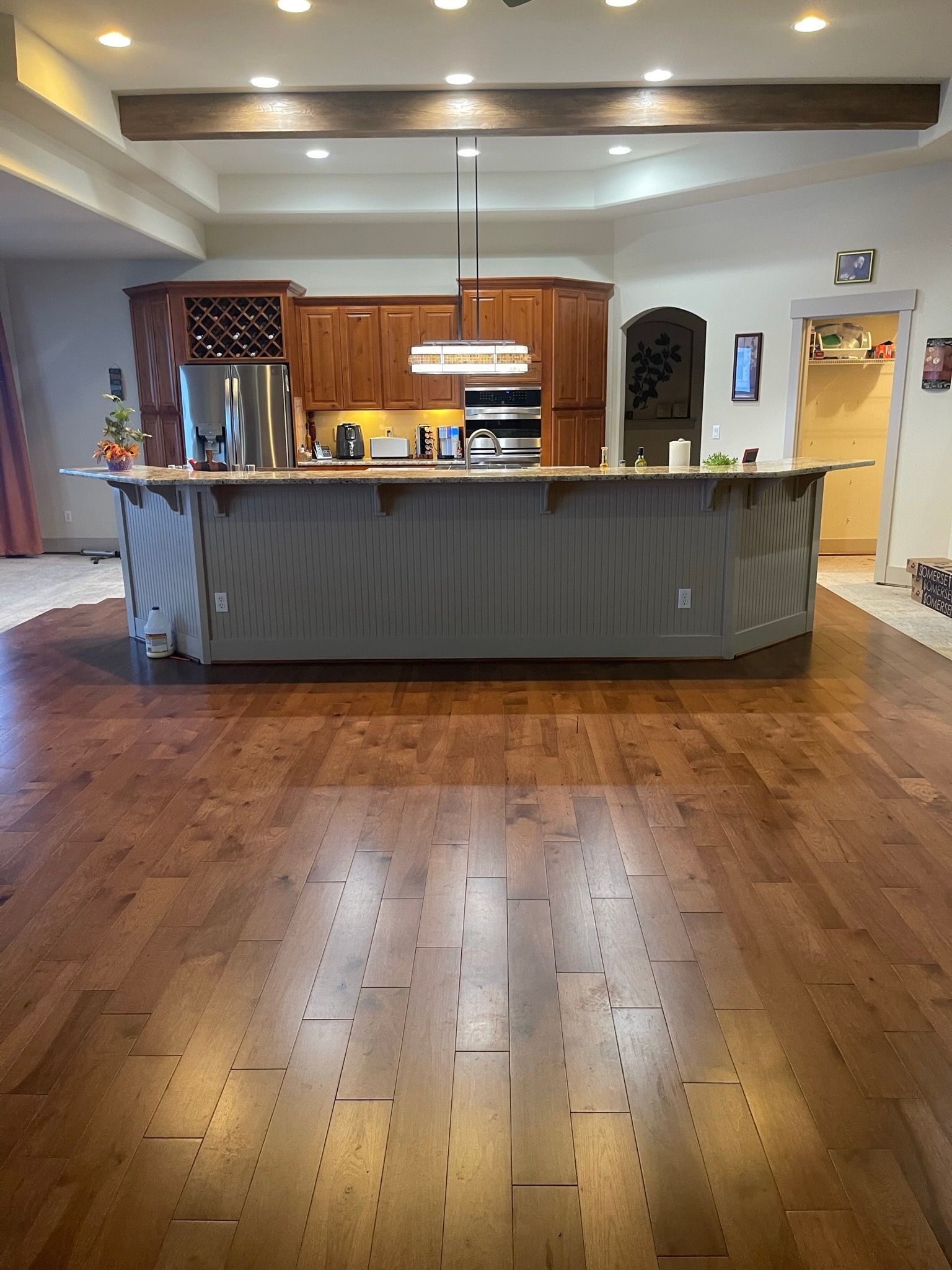A large kitchen island with a grey paneled front sits on wide-plank hardwood floors, with wooden cabinets in the back.