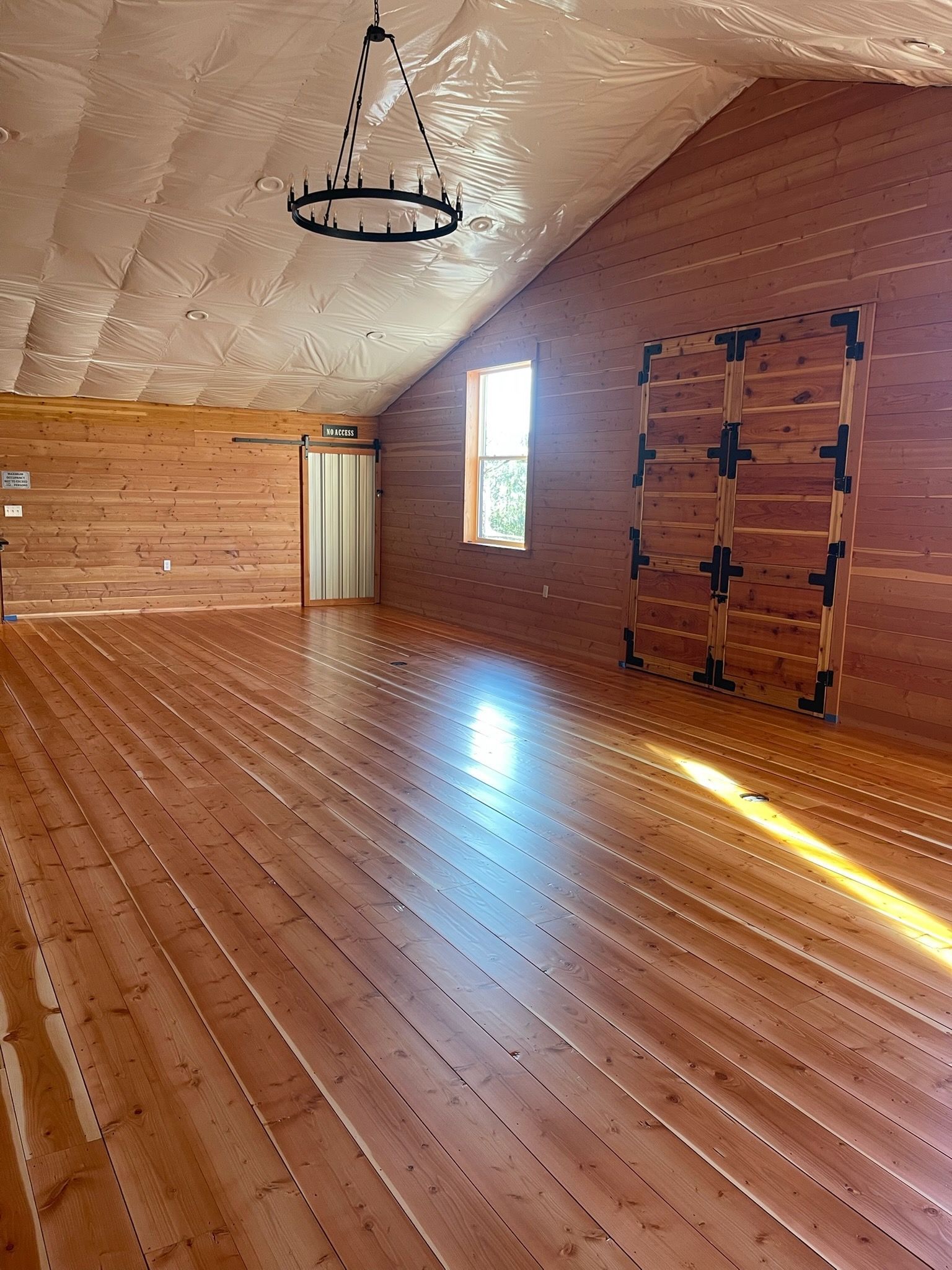 A spacious room with wood-paneled walls and floor, a vaulted ceiling with a circular chandelier, and a gym ladder wall.