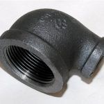 A close up of a black pipe elbow on a white surface.