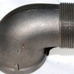 A close up of a metal pipe elbow on a white surface.