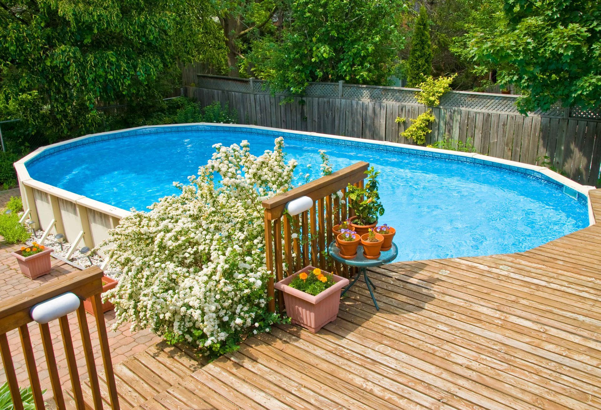 A large swimming pool is surrounded by potted plants and a wooden deck.
