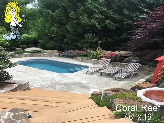 A large Coral Reef swimming pool surrounded by chairs and trees in a backyard.