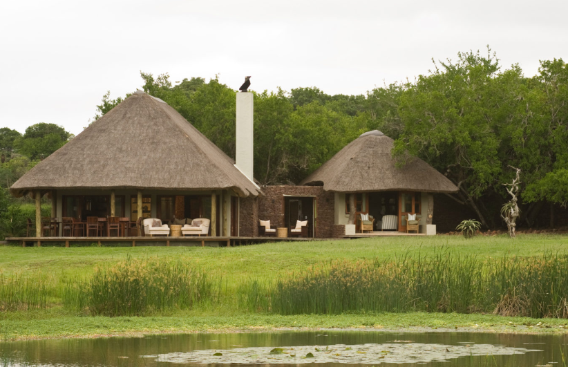 A house with a thatched roof and a pond in front of it
