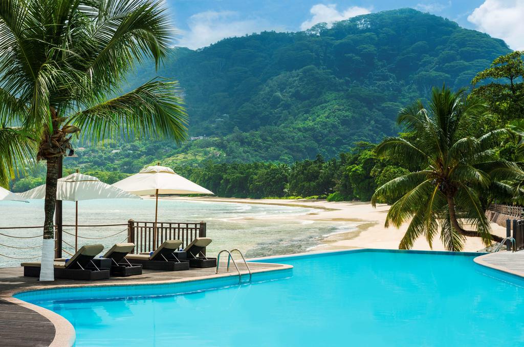 A large swimming pool surrounded by palm trees and chairs with mountains in the background.