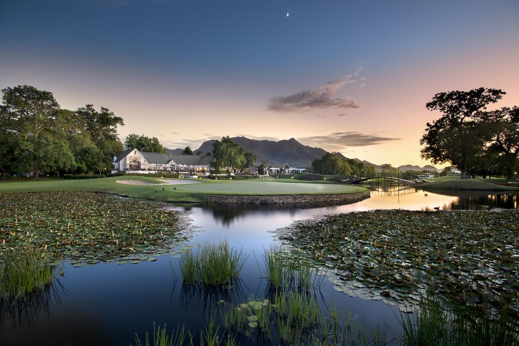A golf course with a pond in the foreground and a house in the background.
