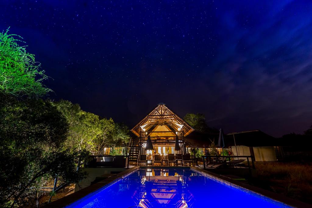 A large swimming pool is lit up at night in front of a house.