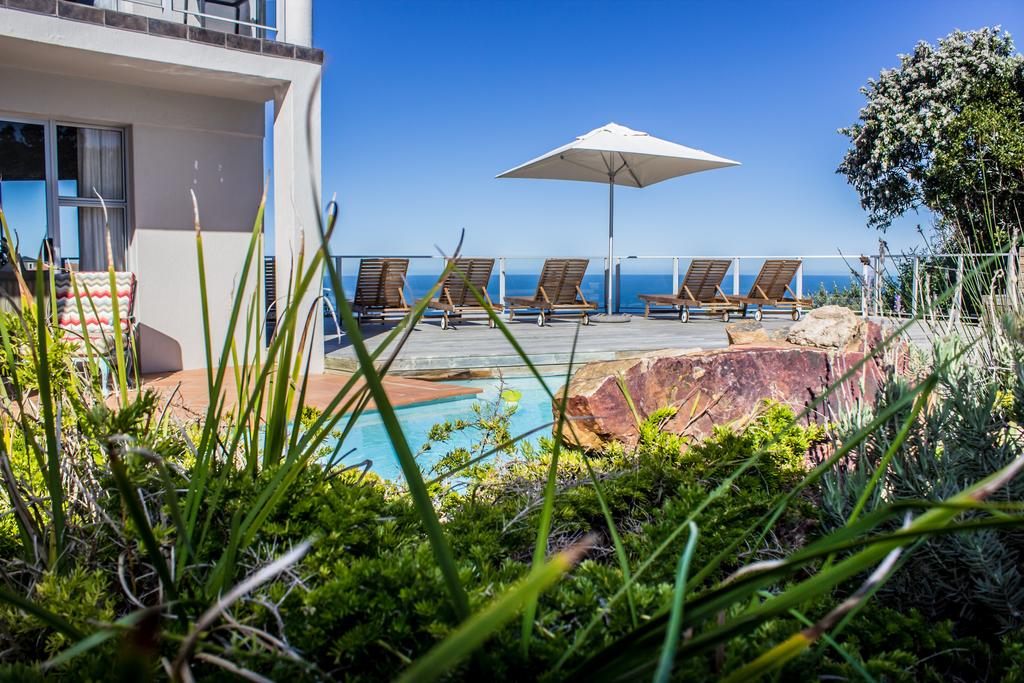 A swimming pool with chairs and umbrellas in front of a house.