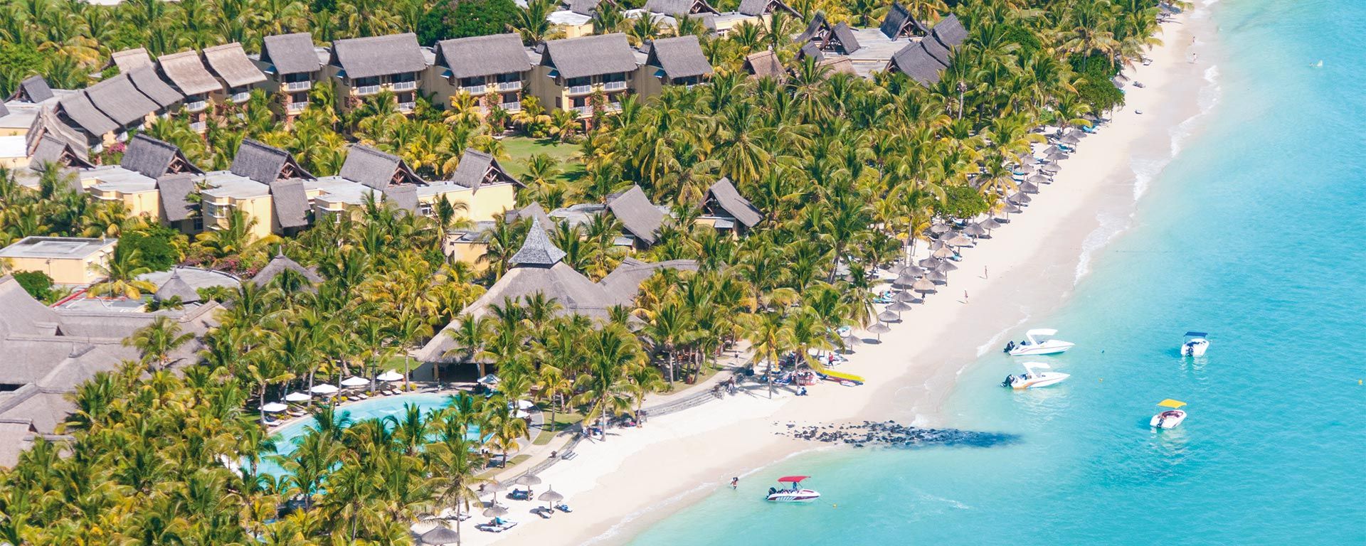 An aerial view of a tropical beach with palm trees and boats in the water.