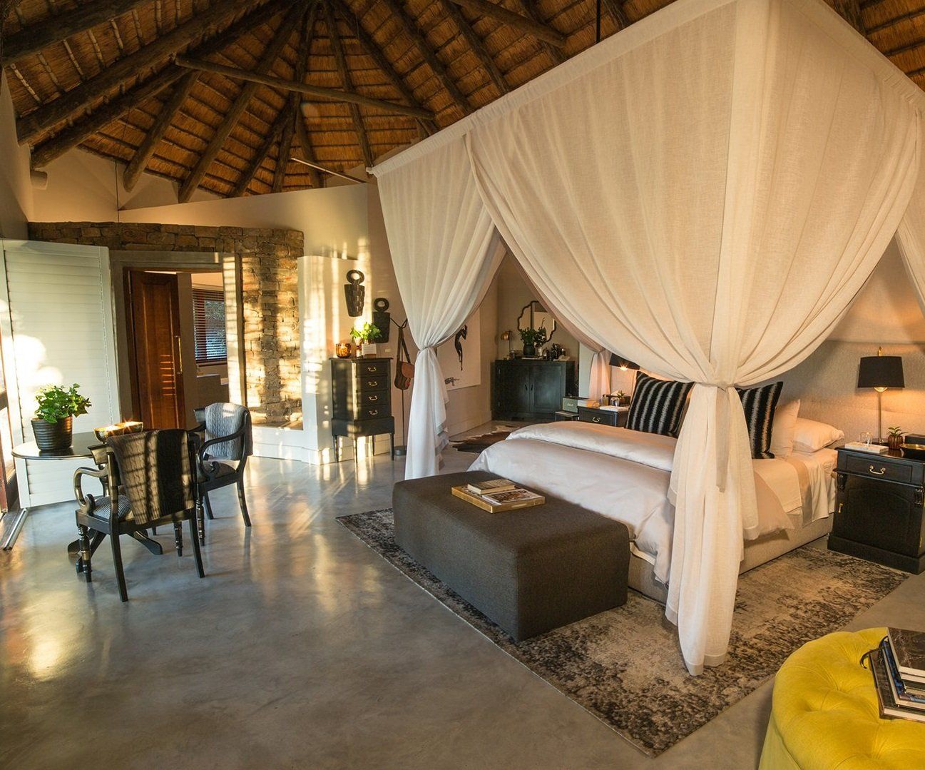 A bedroom with a canopy bed and a yellow ottoman
