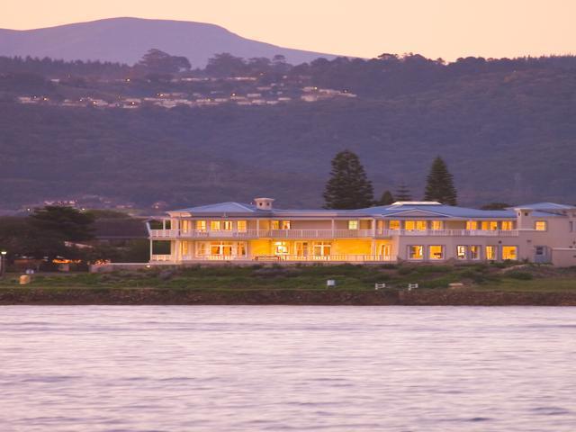 A large house sits on a hill overlooking a body of water
