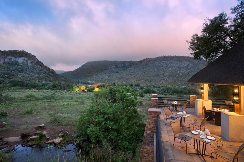 A patio with tables and chairs overlooking a river and mountains.