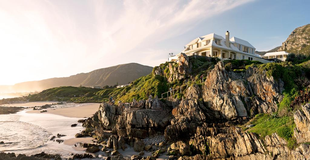 A large white house sits on top of a rocky hill overlooking the ocean.