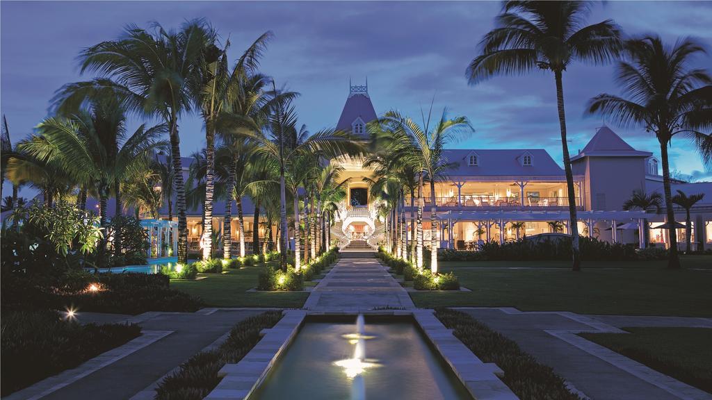 A large white building with a fountain in front of it surrounded by palm trees.
