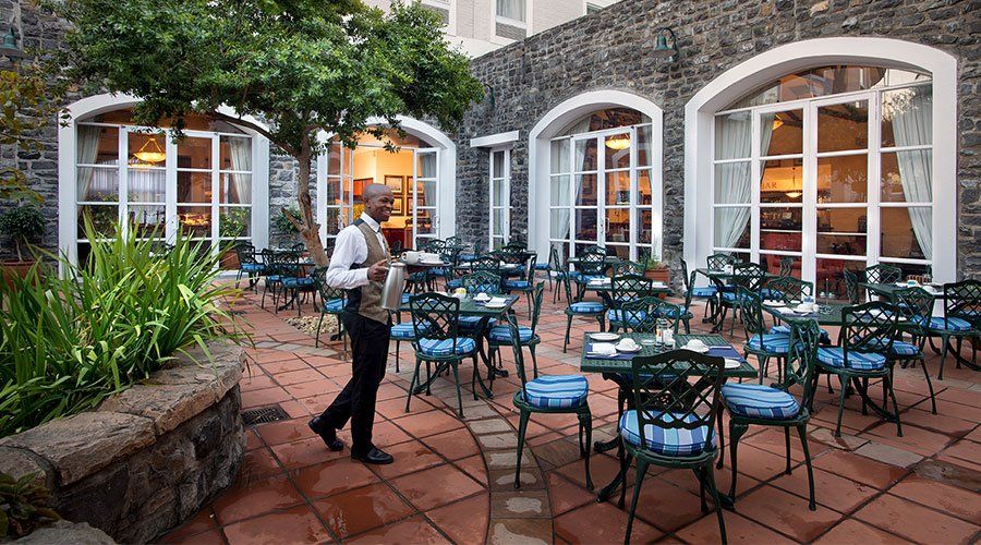 A man is standing in front of a restaurant with tables and chairs.