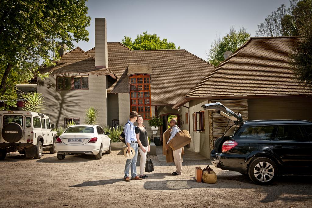 A group of people are standing in front of a house with cars parked in front of it.