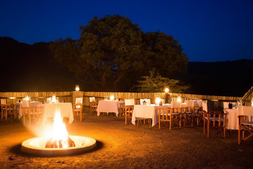A fire pit in the middle of a dining area with tables and chairs.