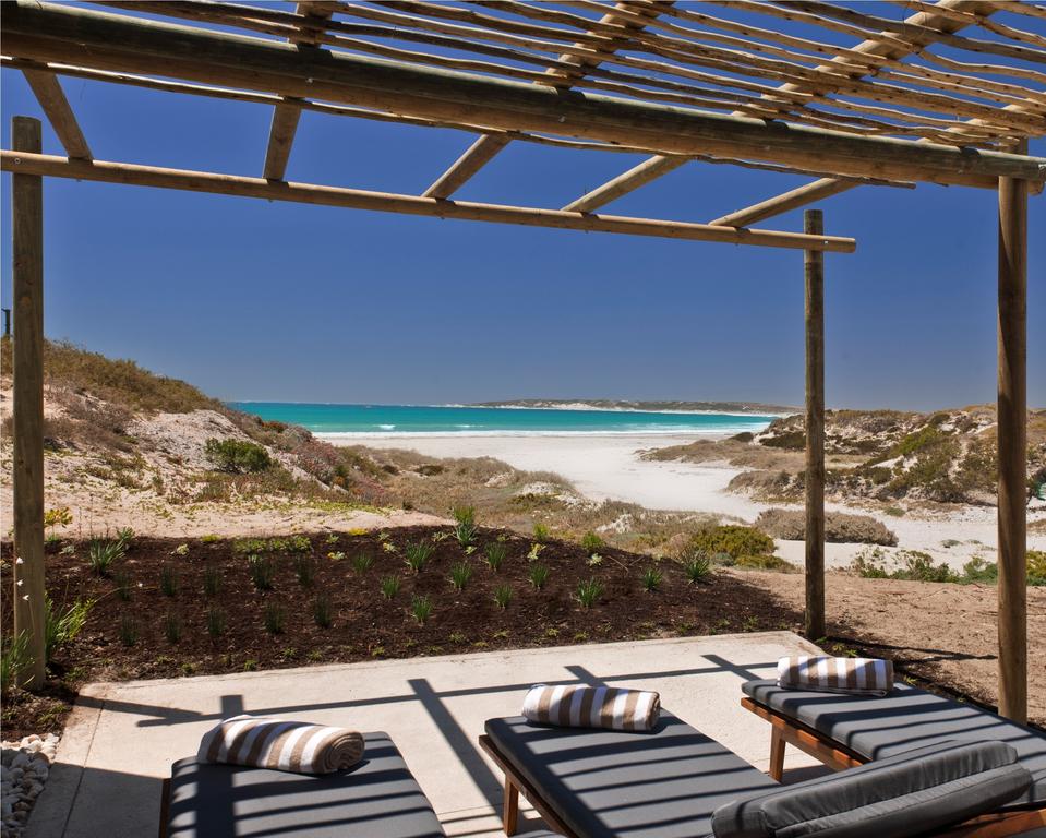 Two lounge chairs under a pergola overlooking a beach