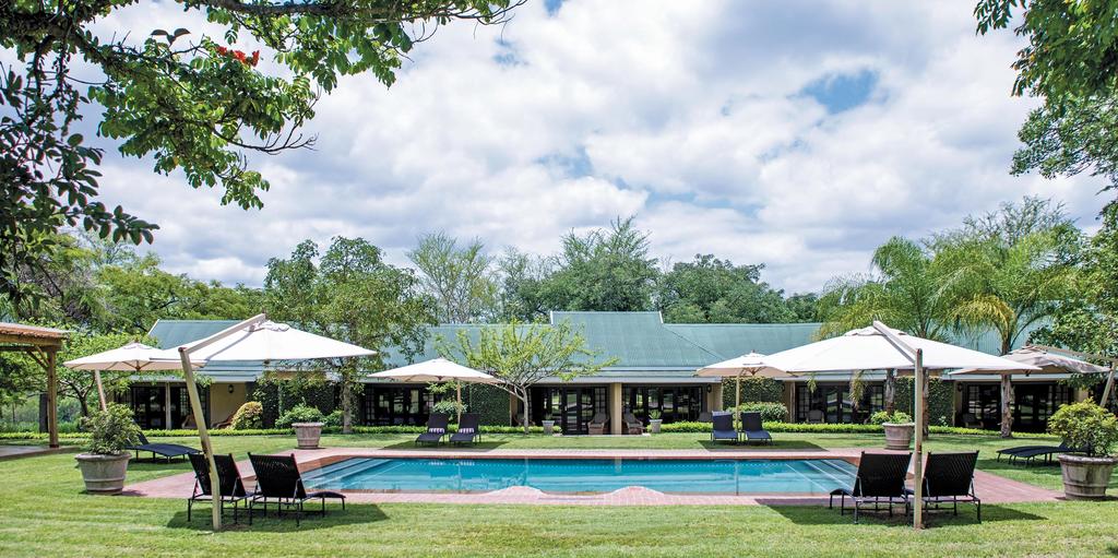 A large swimming pool surrounded by chairs and umbrellas in front of a house.
