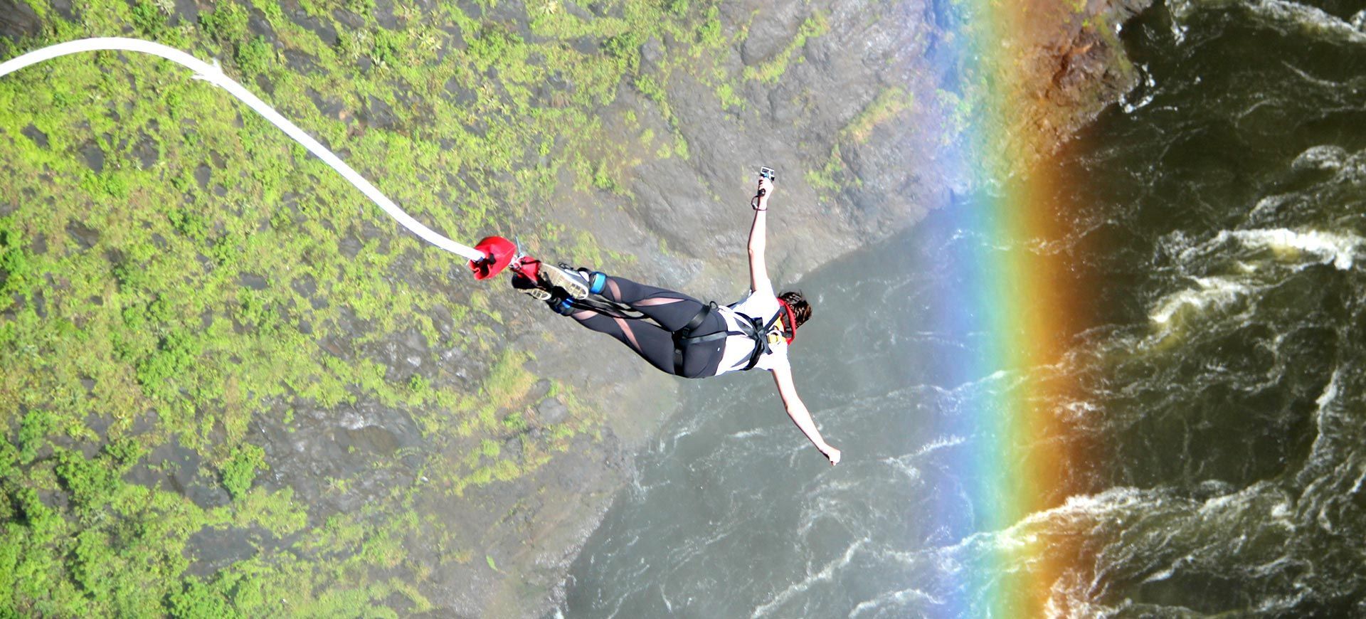 A person is jumping off a cliff into a river with a rainbow in the background.