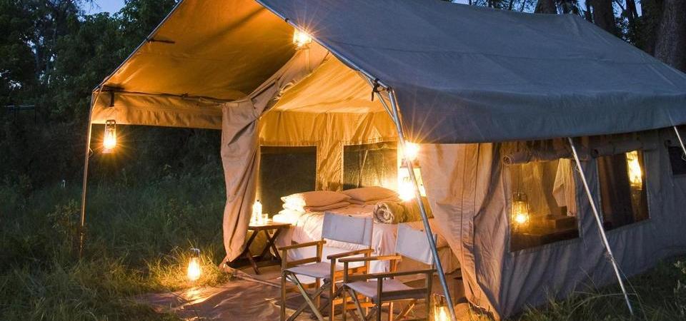 A tent with a bed and chairs in it is lit up at night.